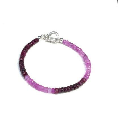 One genuine ruby gemstone beaded bracelet with sterling silver toggle clasps, featuring faceted round rubies ranging from pink to red on a white background, front overview.
