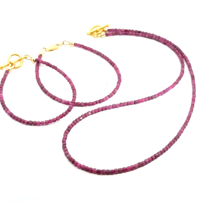 Close-up of faceted ruby cubed beaded bracelets with a matching necklace showing deep red hues and natural shine on a white background, front overview.