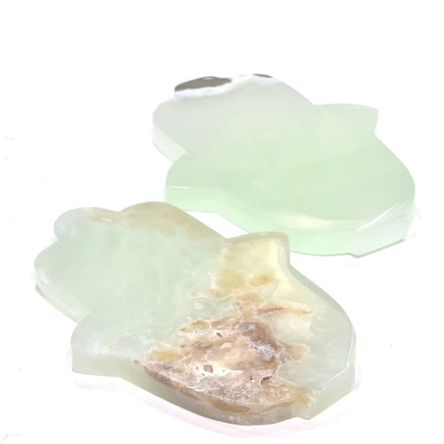 Two pistachio calcite humza gemstone carvings with a pale green to white color and varying shades of brown, displayed on a white background, front overview