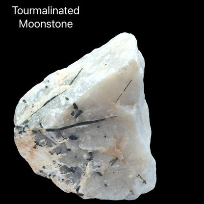 An Extra large raw tourmalinated moonstone specimen 4 pounds with black tourmaline needles through pearlescent white moonstone on a black background, front view.